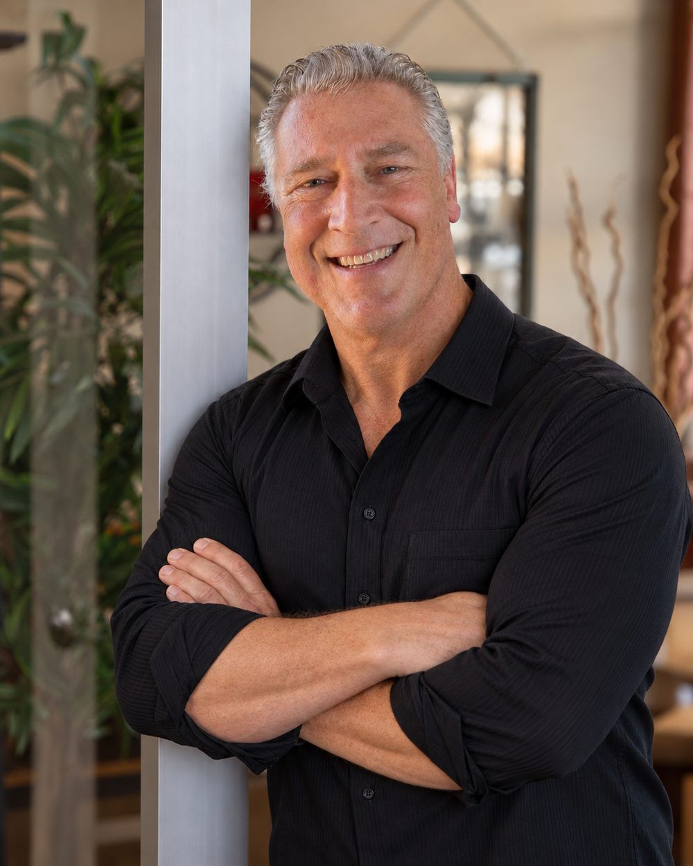 Portrait of Sean Purcell, smiling, with his arms crossed, leaning against a post